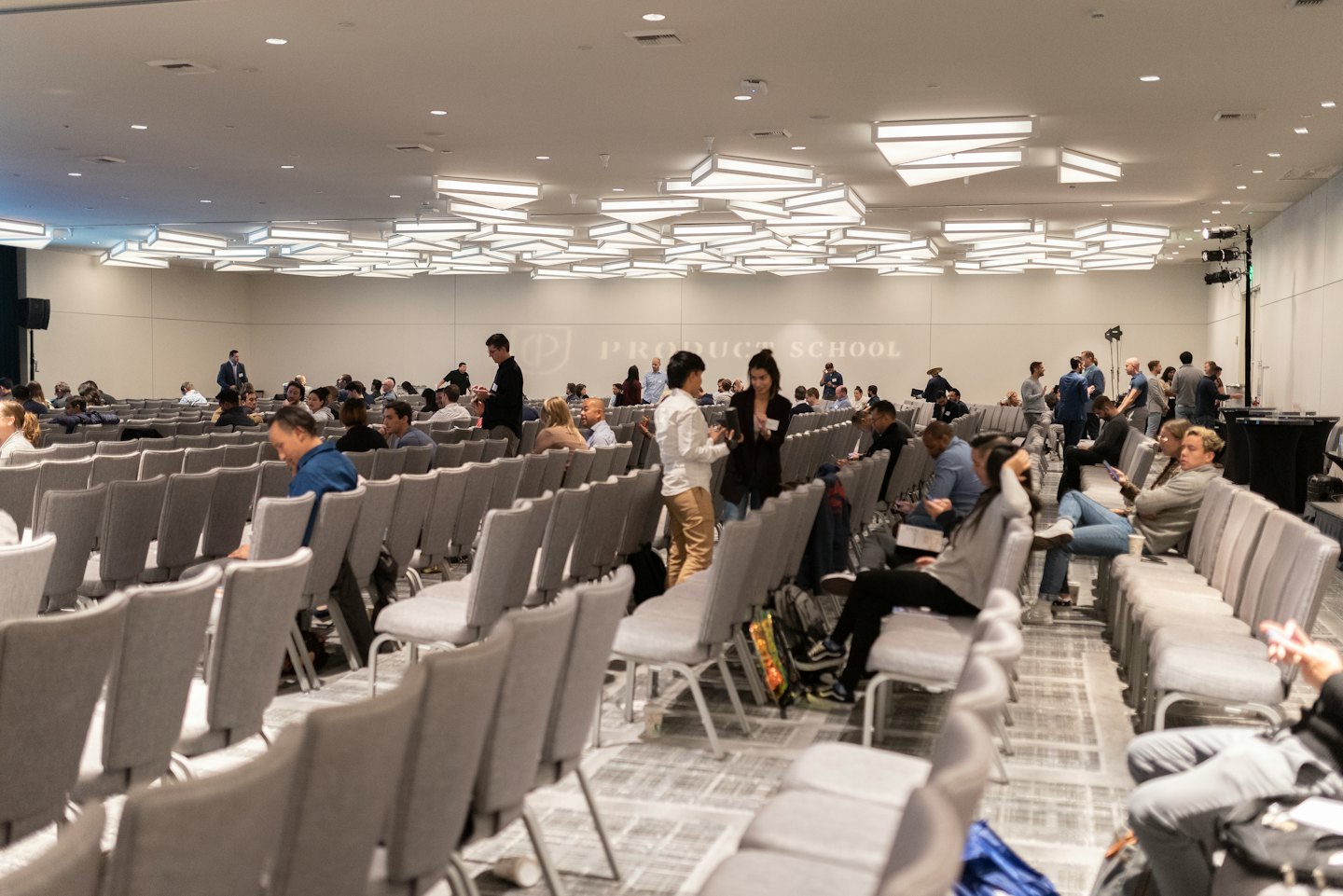 Des adultes diversifiés réseautent et assistent à une conférence dans un hall moderne.